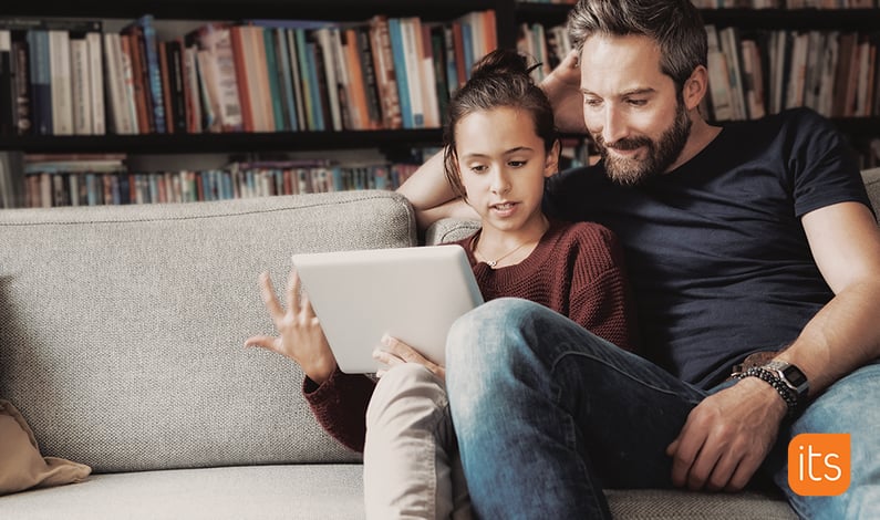 Vater und Tochter sitzen auf der Couch in ihrem Wohnzimmer und schauen gemeinsam auf ein Tablet.