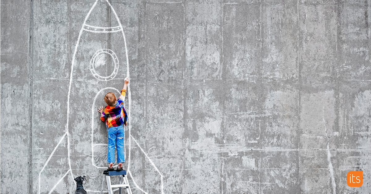 Foto eines Schülers, der mit einem Kreidestift in der Hand vor einer Betonwand steht und ein Raketenschiff zeichnet.